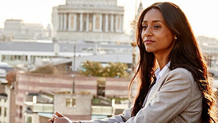 A business professional stands on a rooftop of a city building and gazes into the distance.