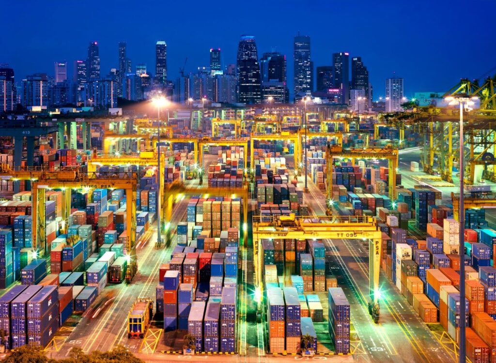 A Singapore shipping terminal loaded with crates, with the Singapore skyline in the background.