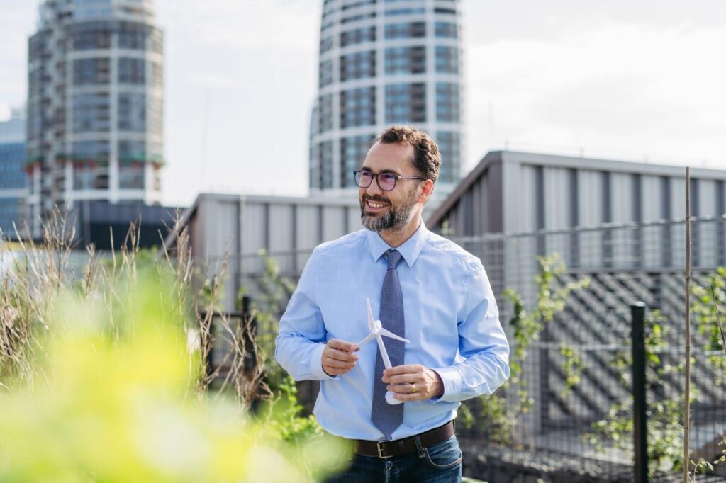 A business person in an urban community garden holds a model of a wind turbine.