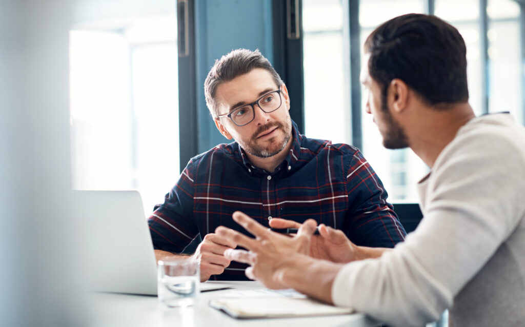 A financial analyst speaks to a client in an office beside an open laptop.