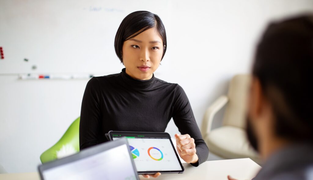 A consultant speaks to a client while holding a tablet containing graphs of data.