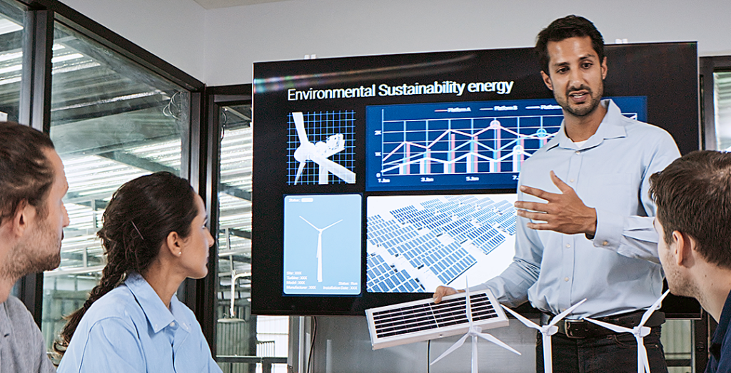 A young professional addressing a group in a conference room delivers a presentation on wind turbines and sustainable energy sources.